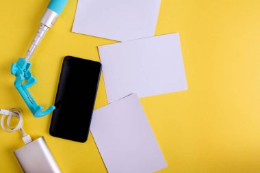 Düz sarı bir arka plan üzerinde monopod, akıllı telefon ve fotoğraflar yatıyordu. seyahat konsepti