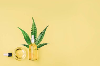 Cbd yağı, pipet, kapsül ve kenevir, sarı bir arka plan üzerinde kenevir yaprağı ile Şişe. Minimal kompozisyon, düz yatıyordu.
