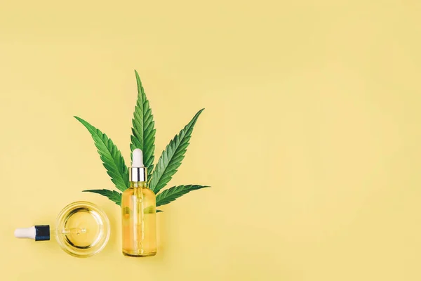 Flaska med CBD-olja, pipett, kapslar och cannabis, hampa blad på gul bakgrund. Minimal komposition, Flat Lay. — Stockfoto