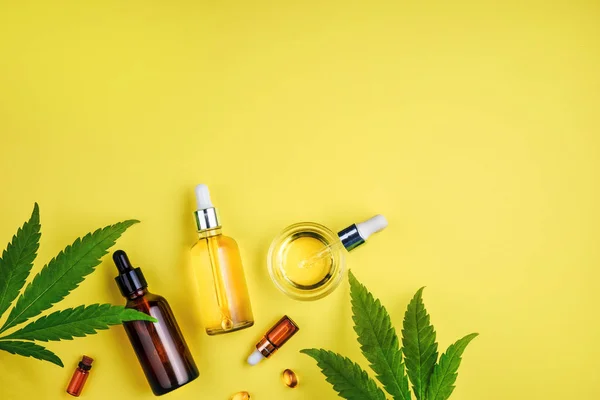 Botellas con aceite de CBD, un gotero y cannabis de hoja sobre un fondo amarillo. Concepto cuidado de belleza con aceite de cáñamo —  Fotos de Stock