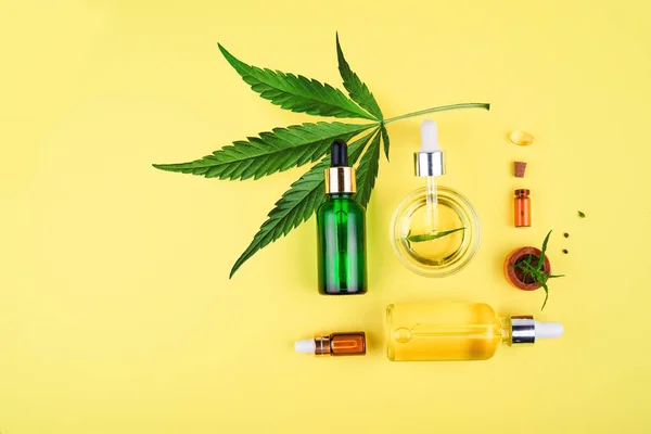 Різні скляні пляшки з CBD OIL, настойкою THC і листям канабісу на жовтому тлі. Плоский простір, мінімалізм. Косметика CBD олія . — стокове фото