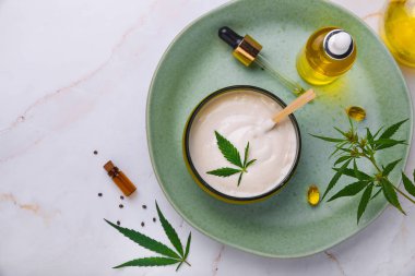 CbD yağı ile tıbbi krem Bankası, kenevir yağı şişesi, kapsüller, yeşil bir tabakta. Düz döşeme, üst görünüm.
