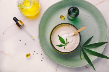 CbD yağı ile tıbbi krem Bankası, kenevir yağı şişesi, kapsüller, yeşil bir tabakta. Düz döşeme, üst görünüm.