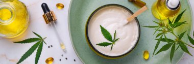 CbD yağı ile tıbbi krem Bankası, kenevir yağı şişesi, kapsüller, yeşil bir tabakta. Düz döşeme, üst görünüm.