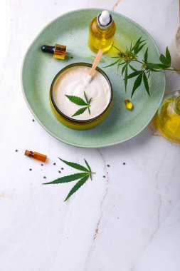 CbD yağı ile tıbbi krem Bankası, kenevir yağı şişesi, kapsüller, yeşil bir tabakta. Düz döşeme, üst görünüm.