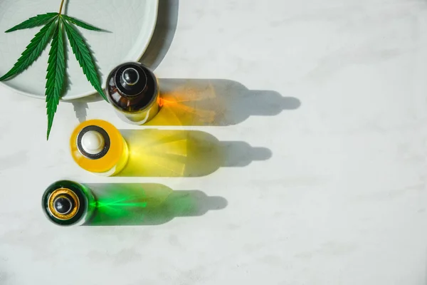 不同的玻璃瓶与Cbd油，刺剂和大麻叶在黄色背景。平铺 — 图库照片