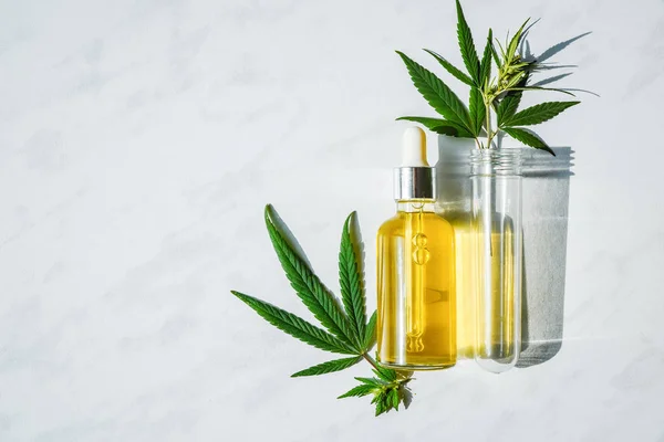 Glass bottle with cannabis oil and a test tube with hemp leaves on a marble background. Copy space. — Stock Photo, Image