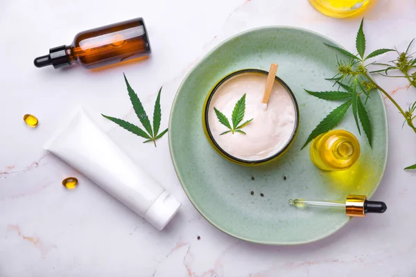 Cosmetics with cannabis oil on a turquoise plate on a light marble background. Copy space, mockup. — Stock Photo, Image