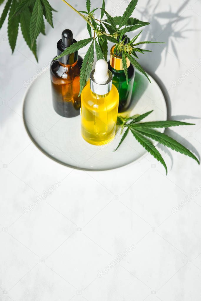 Different glass bottles with CBD OIL, THC tincture and cannabis leaves on yellow background. Flat lay