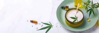 CbD yağı ile tıbbi krem Bankası, kenevir yağı şişesi, kapsüller, yeşil bir tabakta. Düz döşeme, üst görünüm.