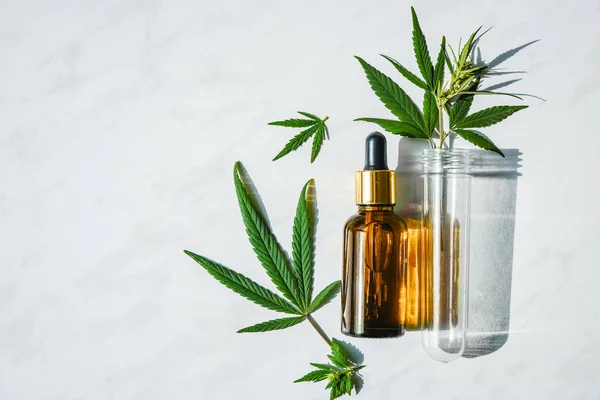 Glass bottle with cannabis oil and a test tube with hemp leaves on a marble background. Copy space. — Stock Photo, Image