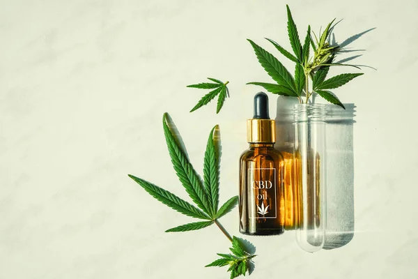 Glass bottle with cannabis oil with label and a test tube with hemp leaves on a marble background. Copy space. — Stock Photo, Image