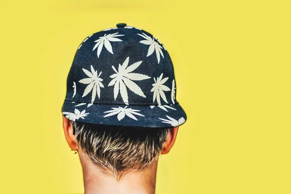 Meisje met zonnebril en pet met bladeren van marihuana rookt op gele achtergrond — Stockfoto