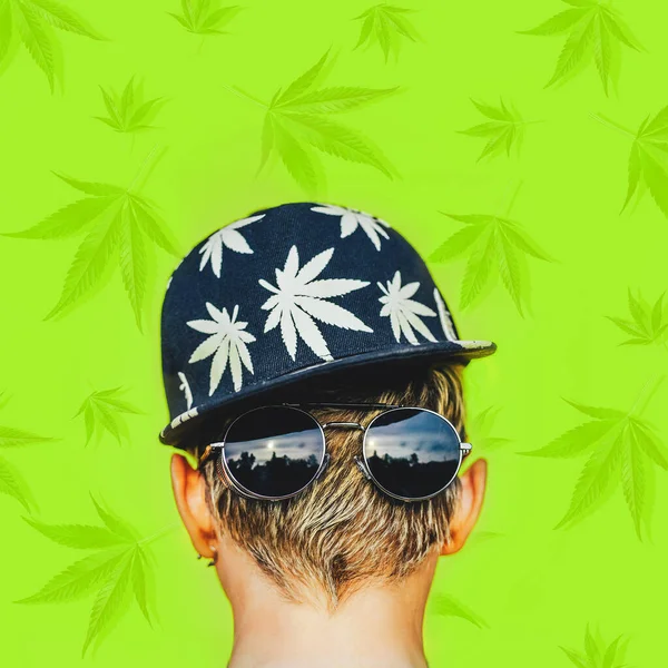 Girl in sunglasses and baseball cap with leaves of marijuana on green background — Stock Photo, Image