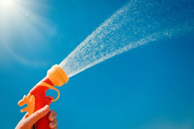 Mavi gökyüzünün arka planında su sıçraması olan sarı hortumu tutan eller.