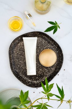 Tuba ve krema kavanozu CBD yağı, THC tentür ve mermer zemin üzerinde kenevir yaprakları. Düzlük, minimalizm. Kozmetik CBD yağı. Kenevir yağı ve marihuana yapraklı krema.