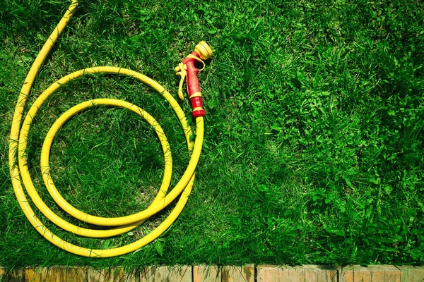 A yellow hose with a nozzle lies on a green lawn folded in rings on the garden. The concept of landscaping and park care. Copy space. Flat lay