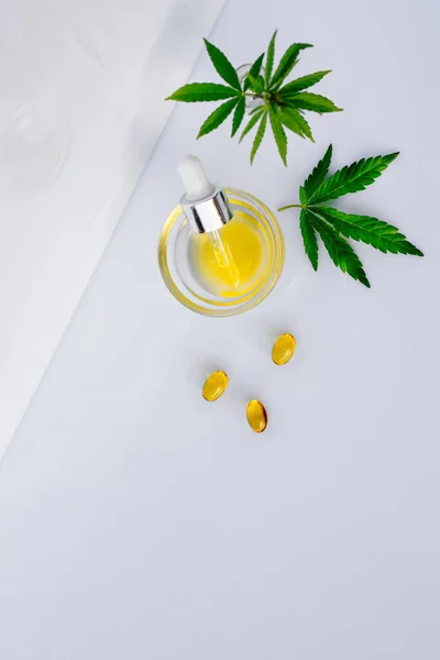 Óleo de CBD farmacêutico e cápsulas em uma mesa de laboratório branca com folhas de cannabis — Fotografia de Stock