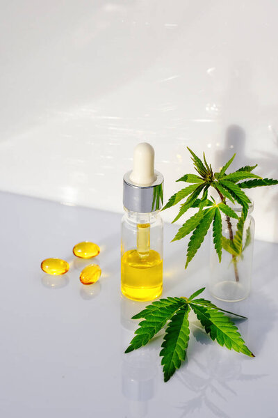 Стеклянная бутылка с маслом CBD, настойка ТГК и листья конопли на белом фоне лаборатории