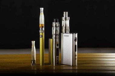 Popular vaping e cig devices mod.electronic cigarette over a wooden background. vaporizer e-cig old device model.  clipart