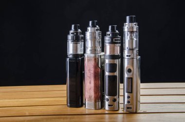 Popular vaping e cig devices mod.electronic cigarette over a wooden background. vaporizer e-cig old device model.  clipart