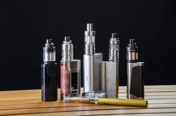 Popular vaping e cig devices mod.electronic cigarette over a wooden background. vaporizer e-cig old device model. 