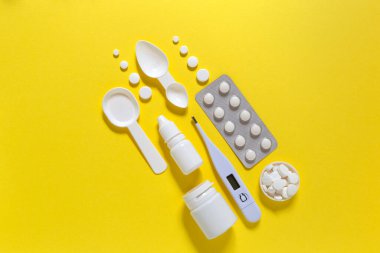 Çapraz düzlüğe yerleştirilmiş tıbbi tedavi seti fotokopi alanı ile yatıyordu. İlaçlar, haplar, termometre, takviye, sarı arka planda burun damlaları.. 