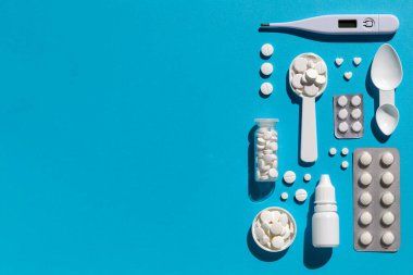 Beyaz tıbbi tedavi seti düz yatıyordu. Termometre, haplı şişe, burun damlası, mavi arka planda kabarcık.. 