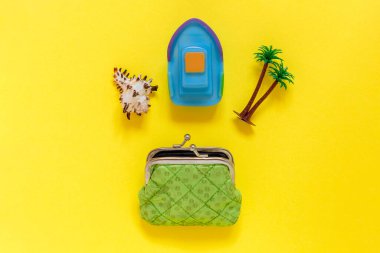 Deniz kabuğu, palmiye ağacı ve tekne sarı arka planda cüzdandan düşüyor. Tatil için para biriktiriyorum