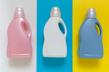 Parlak arka planda üç renkli çamaşır tozu kabı. Mavi, sarı, turuncu ve beyaz deterjan şişeleri