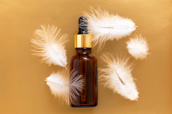 Altın arka planda beyaz tüylü pipetli yağ şişesi. Cilt bakımı kavramı