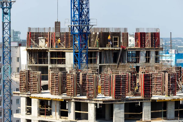Builders are working on a construction site, assembling the frame of a high-rise building from rebar, cement blocks and other building materials. Active urban development and summer constructions