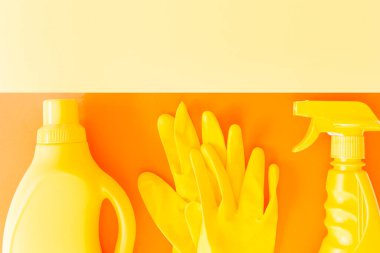 Sarı temizlik seti. Şişeler ve lastik eldivenler turuncu arka planda, sarı fotokopi alanı ile düzdü. Bahar temizliği konsepti, temizlik.