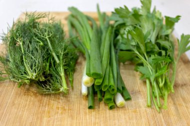 Maydanoz, dereotu, kesme tahtasındaki soğan, ahşap kahverengi masa. Taze yeşiller