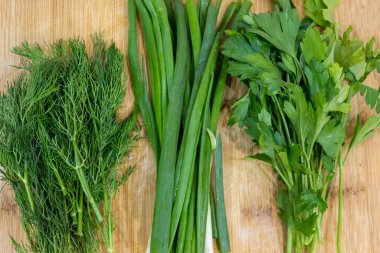 Maydanoz, dereotu, kesme tahtasındaki soğan, ahşap kahverengi masa. Taze yeşiller