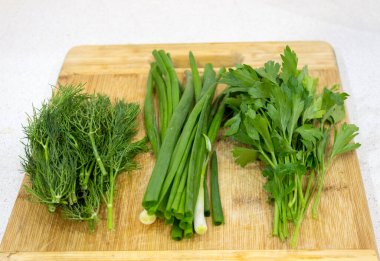 Maydanoz, dereotu, kesme tahtasındaki soğan, ahşap kahverengi masa. Taze yeşiller