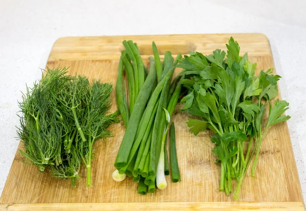 Maydanoz, dereotu, kesme tahtasındaki soğan, ahşap kahverengi masa. Taze yeşiller