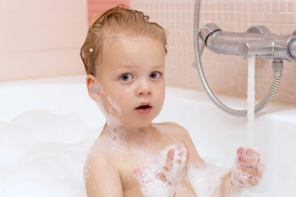 Funny little baby boy with wet curly hair taking a bath with lots of foam playing with water drops and splashes — Stock Photo, Image