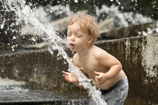 Śmieszne dzieci chłopiec próbuje cauch strumień wody fontanny. Ładny maluch grając w fontannie miasta. — Zdjęcie stockowe