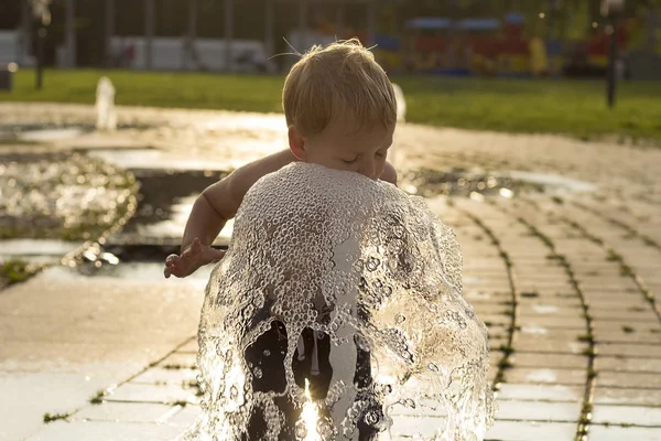 Забавный мальчик, пытающийся залить фонтан водой. Милый малыш играет в городском фонтане — стоковое фото