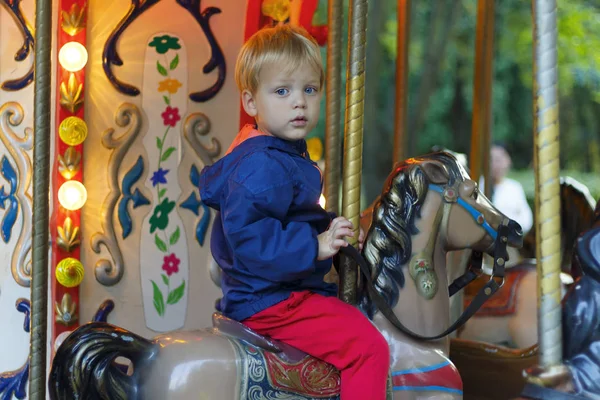 Крупный план счастливый ребенок верхом на игрушечной лошади на карусели. Милый мальчик в парке развлечений. — стоковое фото