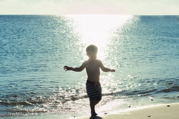 A kisfiú játszik a tengerparton naplemente vagy napfelkelte idején. Boldog nyaralás fogalmának — Stock Fotó