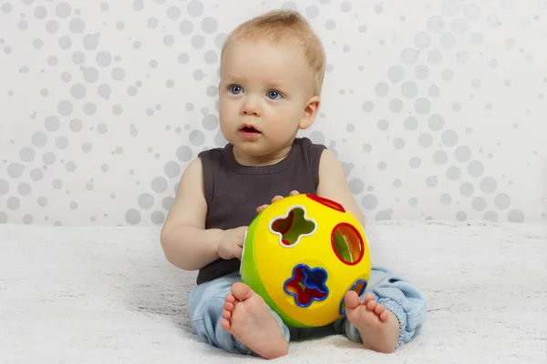 Ritratto di felice carino un anno bambino siedendo sul letto con una palla giocattolo sullo sfondo astratto — Foto Stock