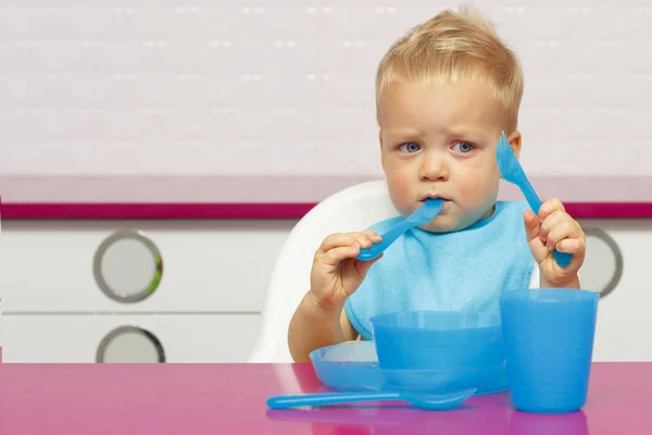 Симпатичный малыш в синем нагруднике на современной кухне . — стоковое фото