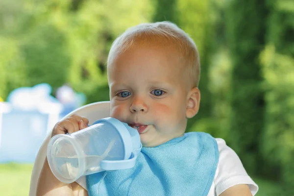 Кумедний малюк п'є воду з пляшки. Він стоїть на зеленому газоні — стокове фото