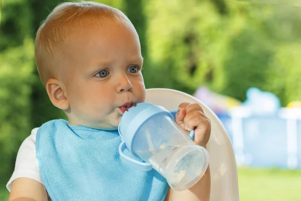 Funny toddler is drinking water from a bottle. It stands on a green lawn Stock Image
