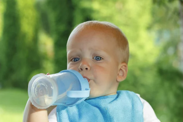Funny toddler is drinking water from a bottle. It stands on a green lawn Royalty Free Stock Photos