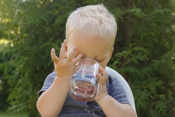 Портрет милого малыша, пьющего воду из стекла в летней среде — стоковое фото