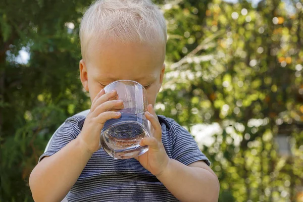 Портрет очаровательного малыша, пьющего воду из стекла на открытом воздухе — стоковое фото