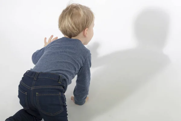 Little boy looking at his shadow in white background with hard light. Studio shot. Copy space — Stock Photo, Image